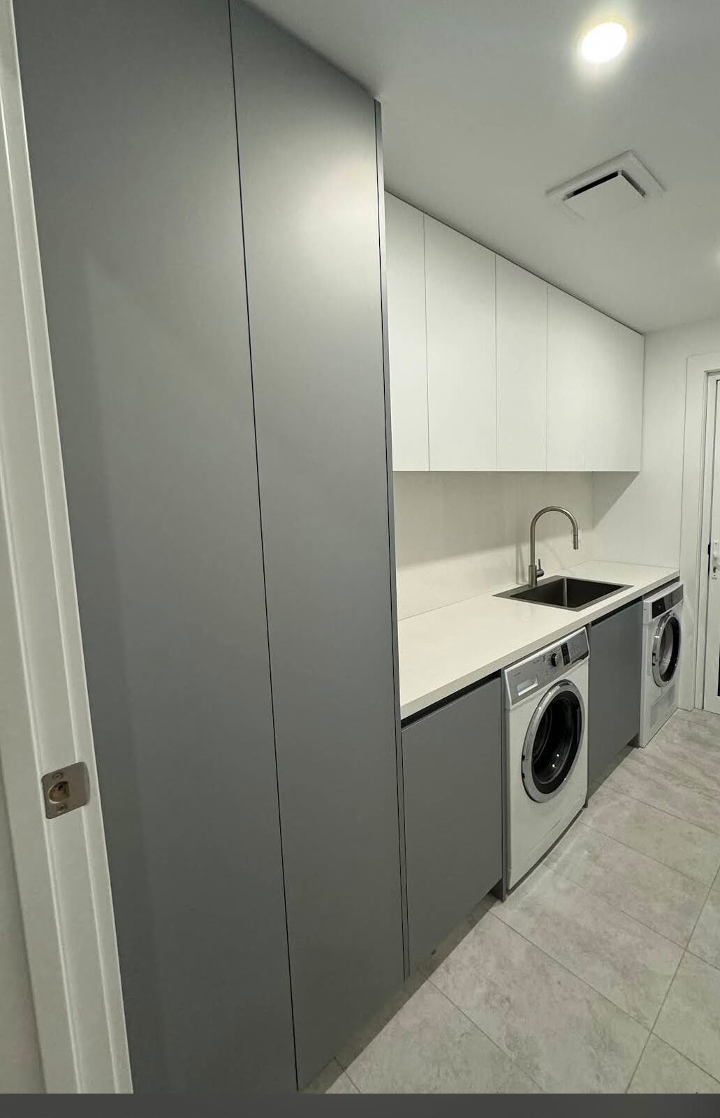 Modern laundry with clean cabinets, sink and appliances